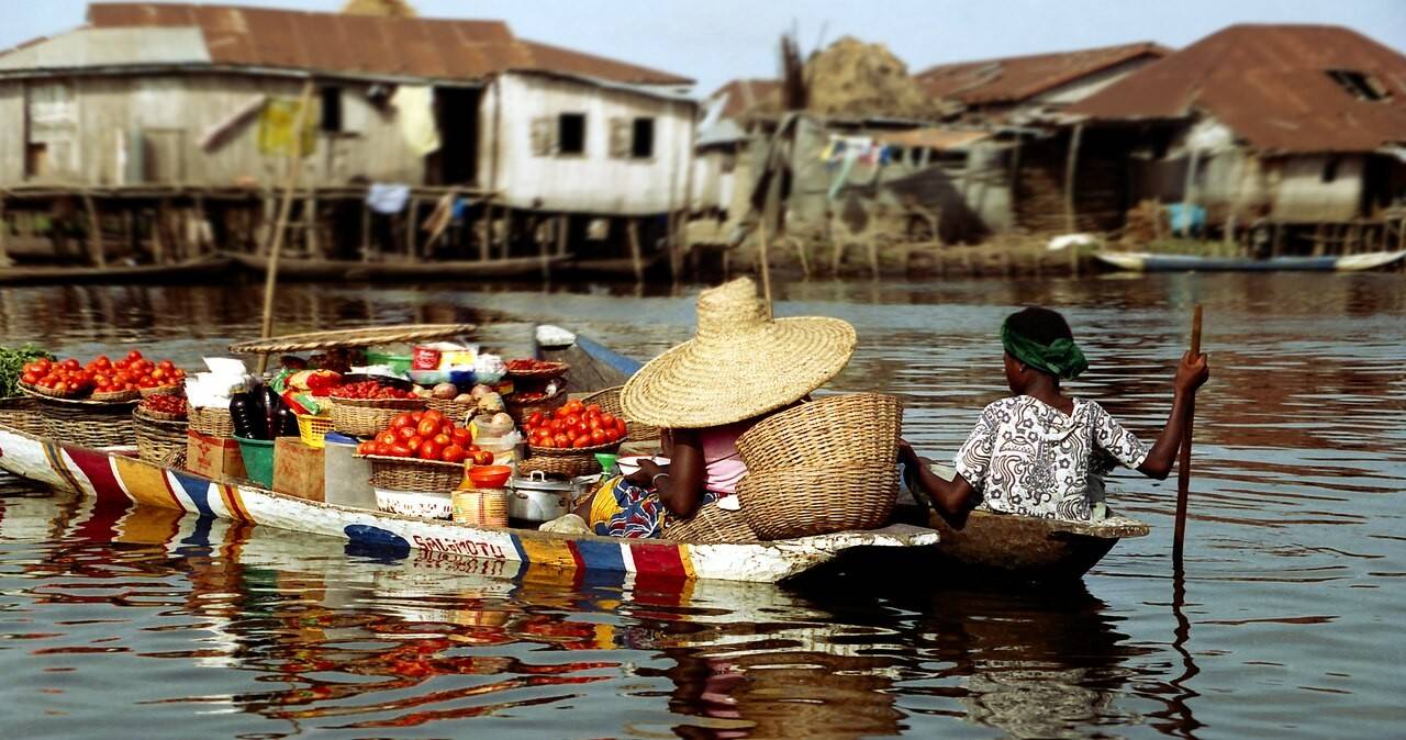 Marché flottant de Ganvié au lever du soleil, femme béninoise vendant des produits locaux en pirogue
