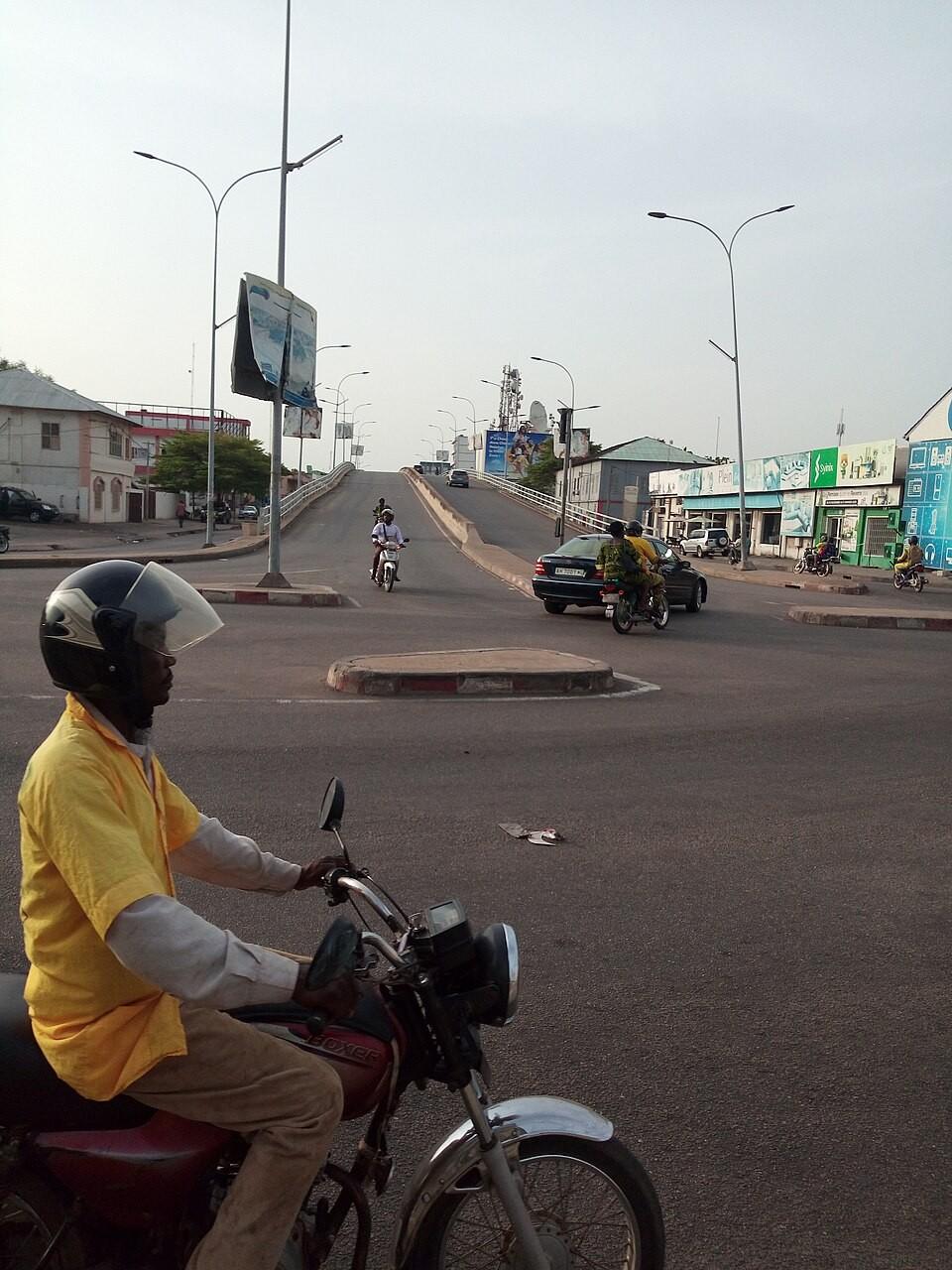 Chauffeur de taxi-moto Zémidjan en chemise jaune sur une route au Bénin, solution de transport économique et authentique