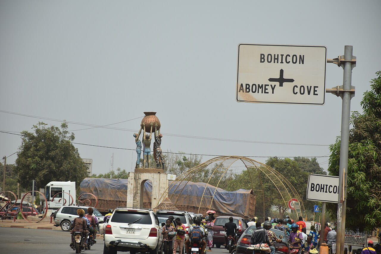 Monument du carrefour de Bohicon avec panneau Abomey Cové, camions et motos pour visiter Bohicon au Bénin