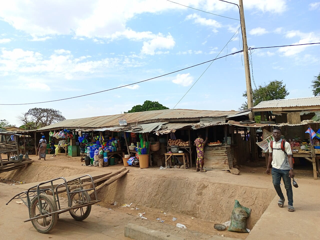 Rue commerçante animée d'un marché à Djougou, au Bénin, avec étals sous toits de tôle et vendeurs