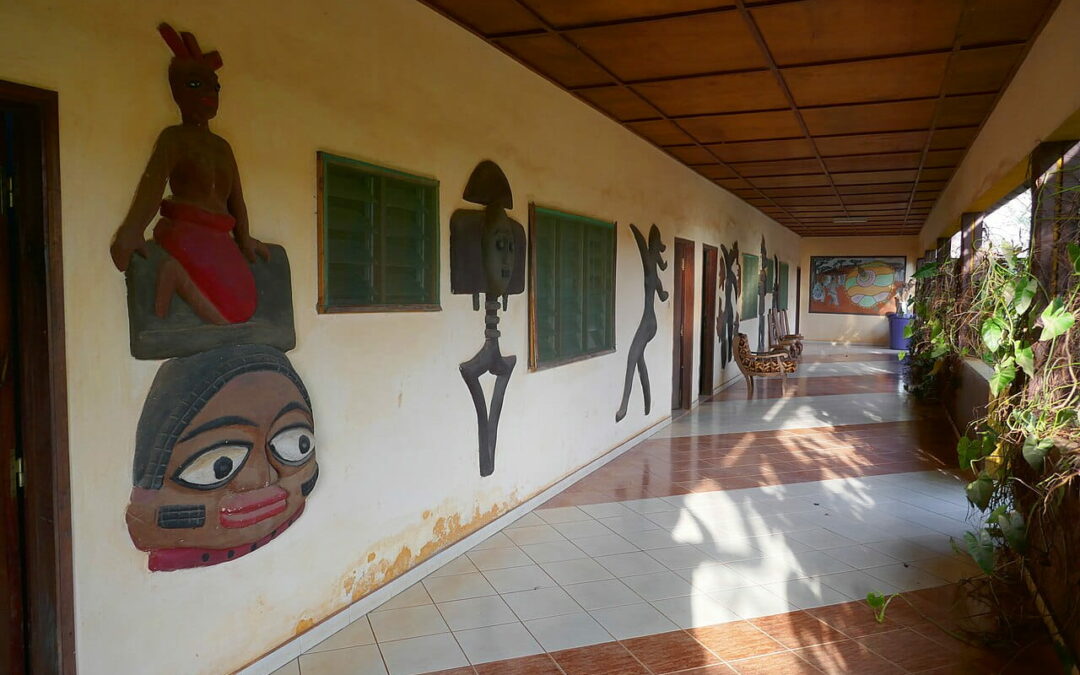 Galerie extérieure de l'Hôtel Chez Monique à Abomey, ornée de masques et sculptures traditionnels, à proximité des palais royaux